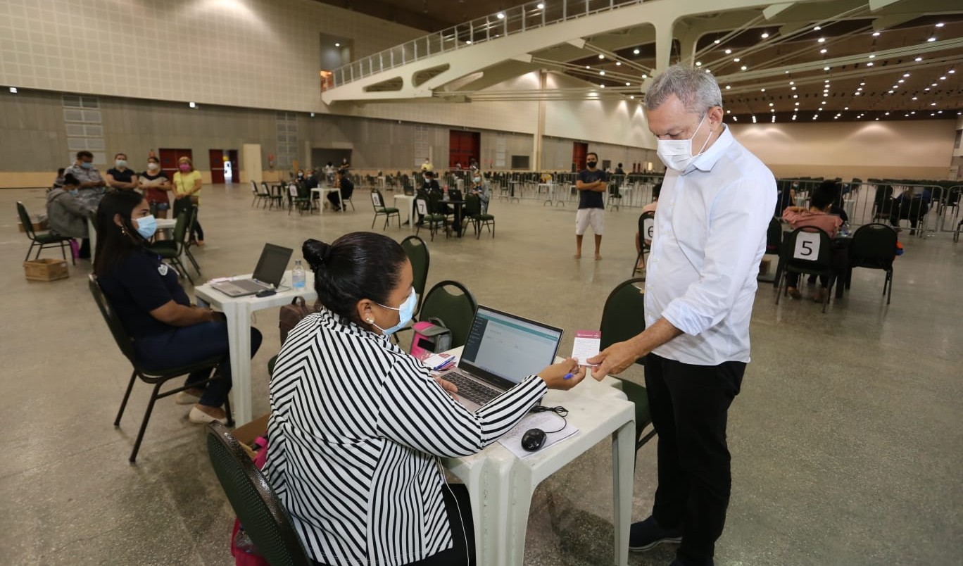 prefeito conversando com uma atendente no centro de eventos e entregando seu cartão de vacina